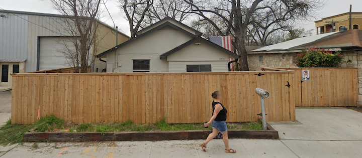 A person walks past a wooden fence in front of a house.