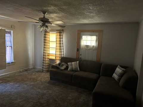 A living room with a brown couch and a ceiling fan.