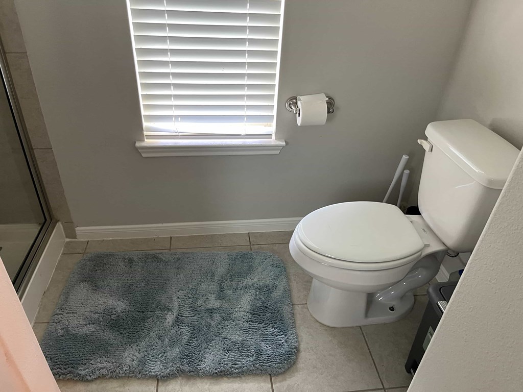 A bathroom with a toilet, a mat on the floor, and a towel on the door.