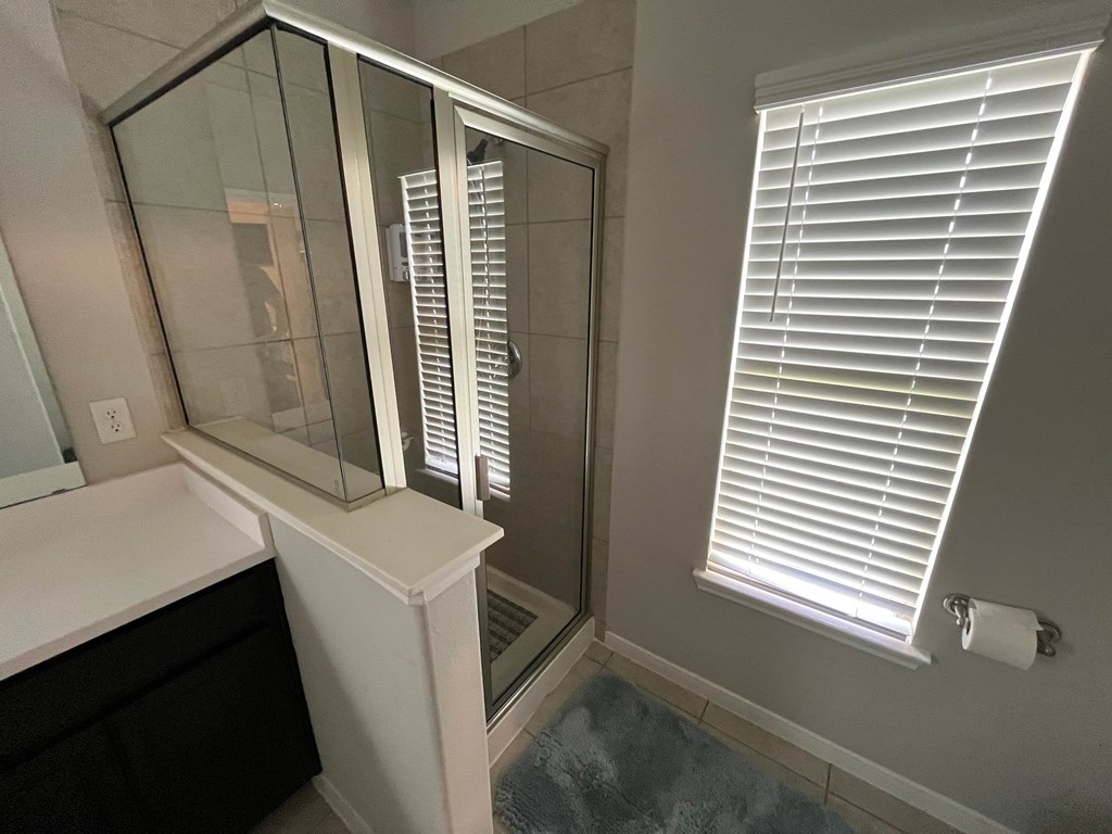 A bathroom with a glass shower door and a window with blinds.