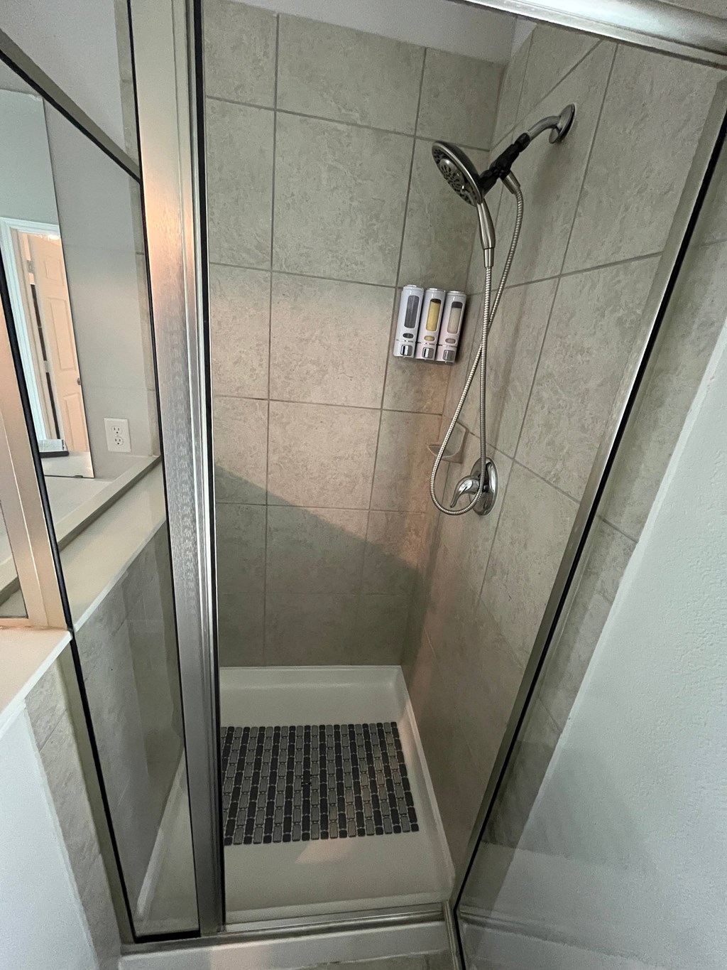 A shower with a glass door and a black and white tiled floor.
