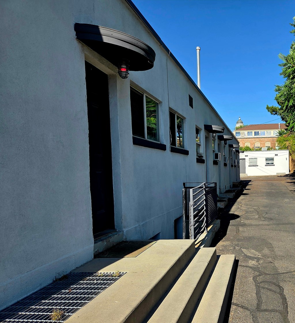 A long white building with a black awning and a metal grate on the ground.