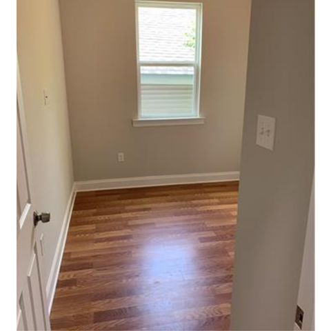 A room with a wooden floor and a window with blinds.
