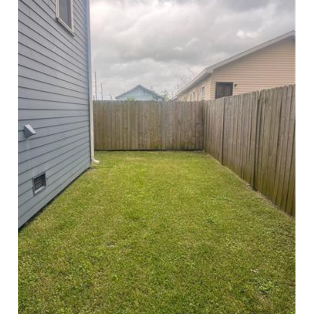 A backyard with a wooden fence and a grey house.