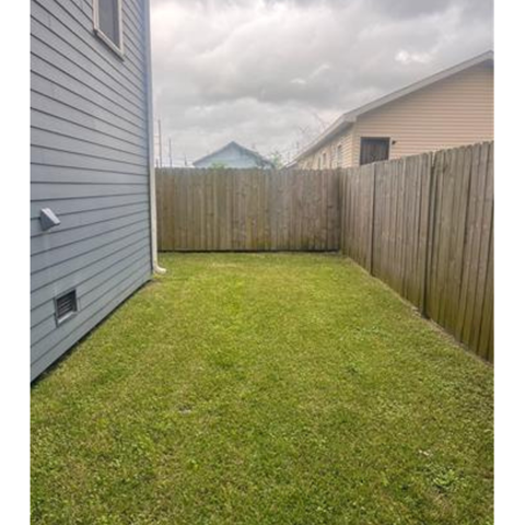 A backyard with a wooden fence and a grey house.
