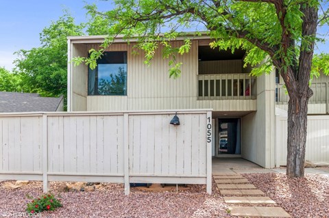 A modern house with a white fence and a tree in front.