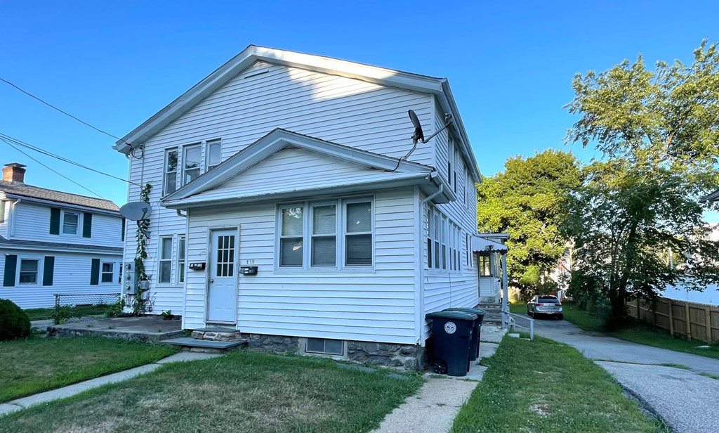 A white house with a blue trash can in front.