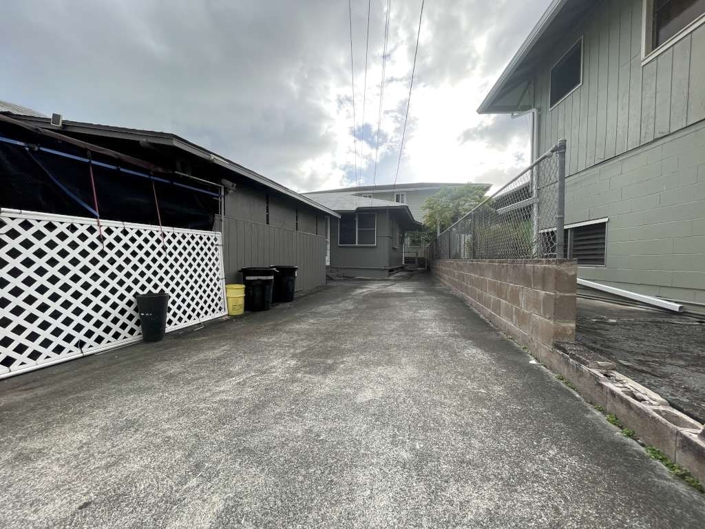 A concrete driveway leads to a house with a white lattice fence on the left.