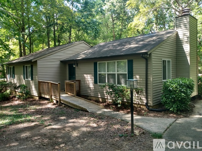 A house with a porch and a chimney is surrounded by trees.