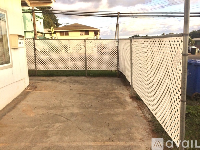 A white fence with a patterned design separates a driveway from a grassy area.
