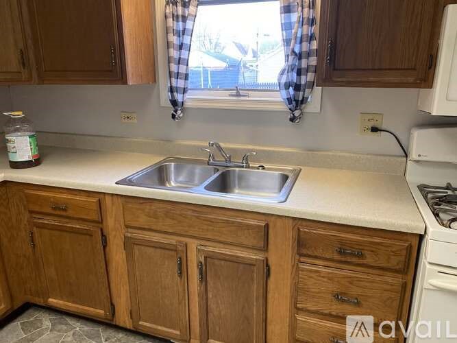 A kitchen with wooden cabinets and a checkered curtain.