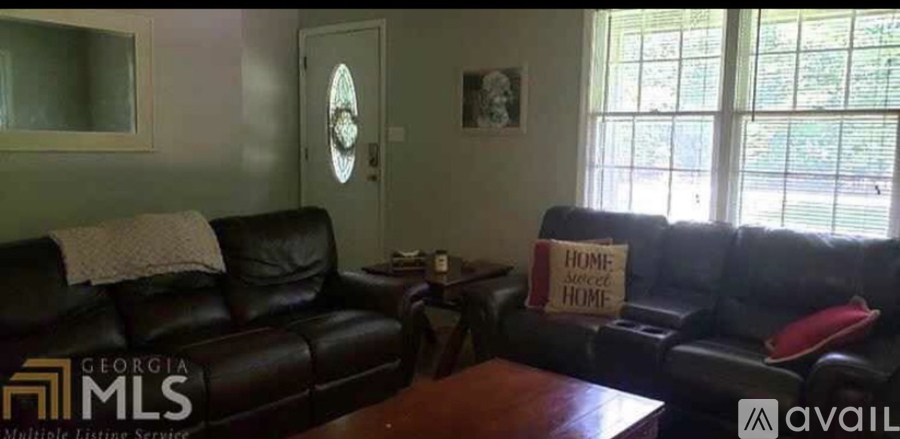 A living room with a black leather couch and a sign that says "Home Sweet Home".