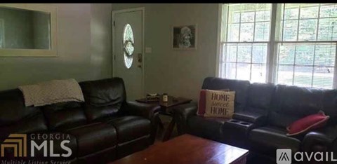 A living room with a black leather couch and a sign that says "Home Sweet Home".