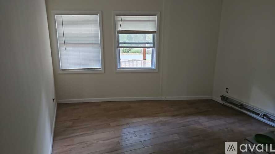A room with wooden flooring and two windows.