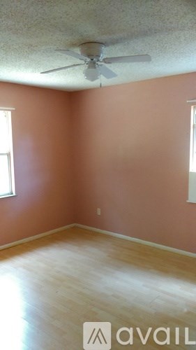 A room with a ceiling fan and light, hardwood floors, and two windows.