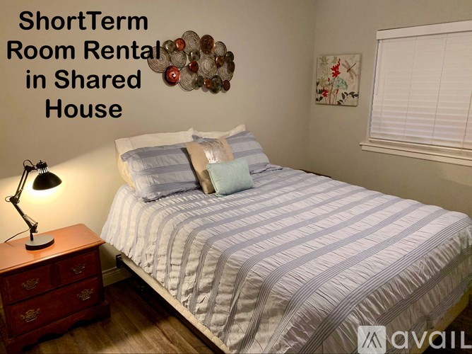 A bedroom with a bed, nightstand, and lamp is advertised for short-term room rental in a shared house.