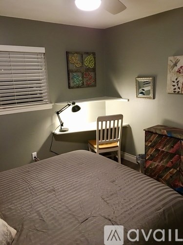 A bedroom with a bed, desk, chair, and a ceiling fan.