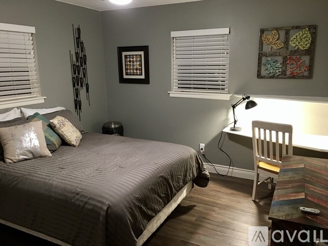A bedroom with a bed, desk, chair, and window with blinds.