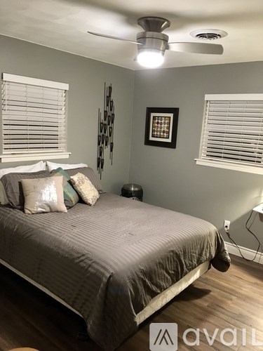 A bedroom with a bed, pillows, a ceiling fan, and a picture on the wall.