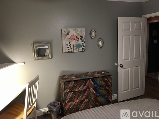 A room with a white door, a chair, a bed, and a wall with pictures and mirrors.