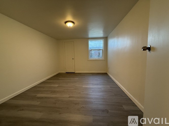 A room with a wooden floor and a window with a view of a fence.