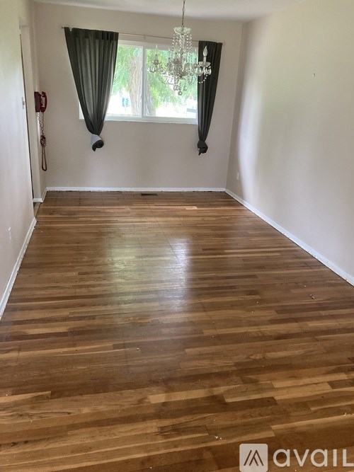 A room with wooden flooring and a window with curtains.