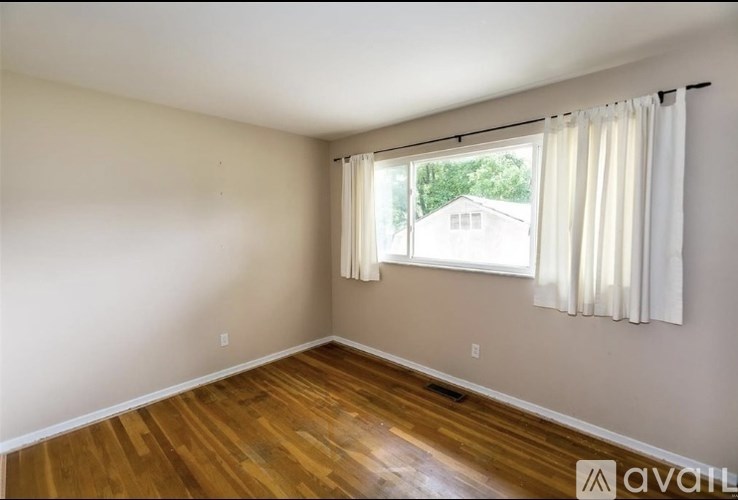 A room with wooden floors and a window with white curtains.