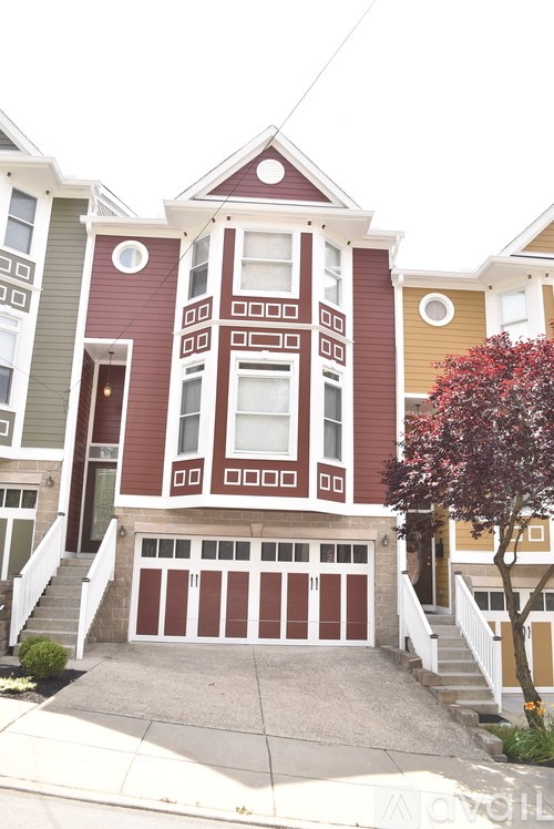 A brown and white two story house with a red tree in front.