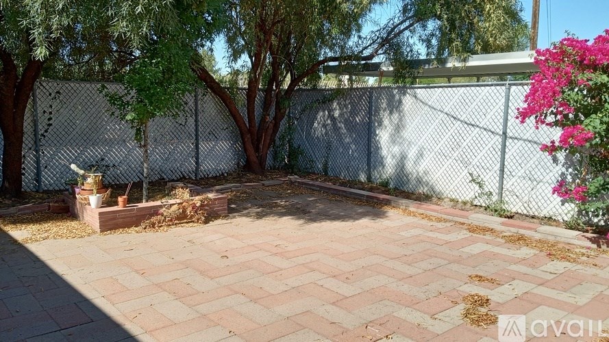A backyard with a fence, a tree, and a brick patio.