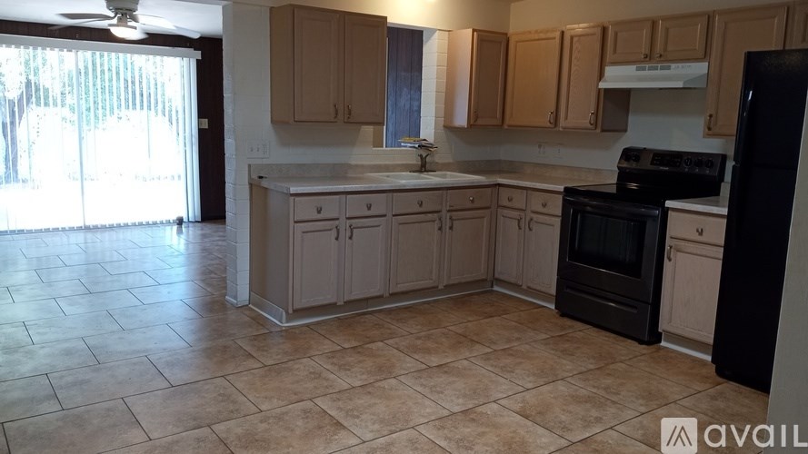 A kitchen with a black refrigerator and a fan.
