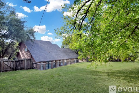 A house with a brown roof and a fence is surrounded by trees.