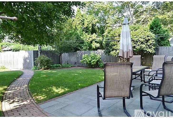 A patio with chairs and an umbrella is surrounded by a fence and trees.