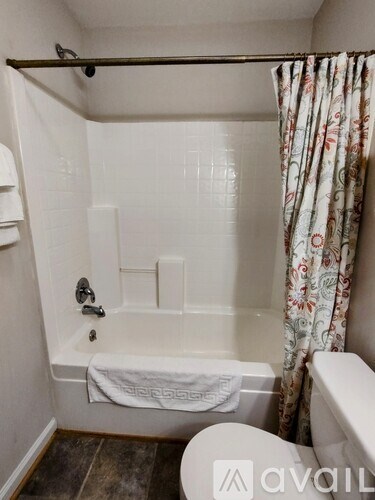 A bathroom with a white toilet, a white tub, and a floral shower curtain.