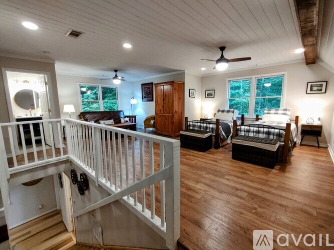 A well-lit room with a staircase and a bedroom with a bed and a dresser.