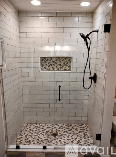 A white tiled shower with a black shower head and hand held shower.