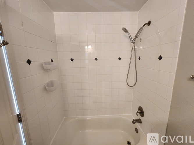 A white tiled shower with a shower head and a bathtub.