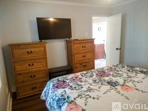 A bedroom with a bed, two dressers, and a television.