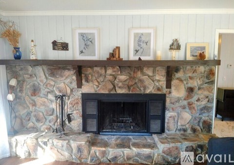 A stone fireplace with a black grate and a mantle above it with picture frames and candles.