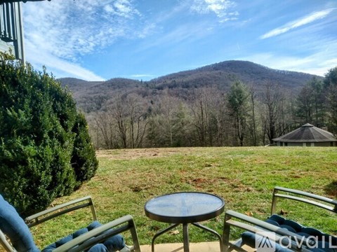 A table and two chairs are set up on a patio overlooking a grassy field and a mountain.