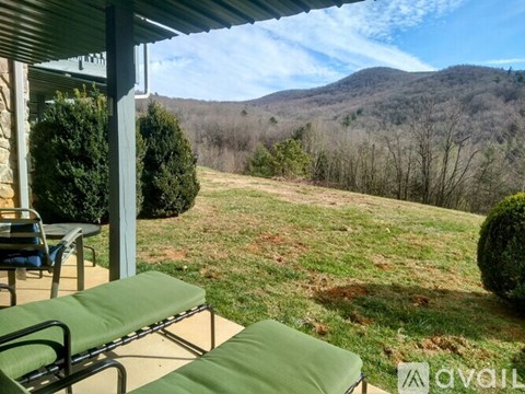 A patio with two green chairs and a table overlooks a grassy hill.