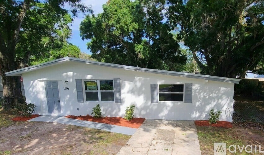 A white house with the number 106 on the front door is surrounded by trees.