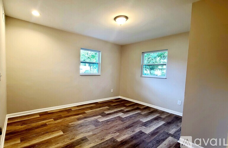 A room with wooden flooring and two windows.