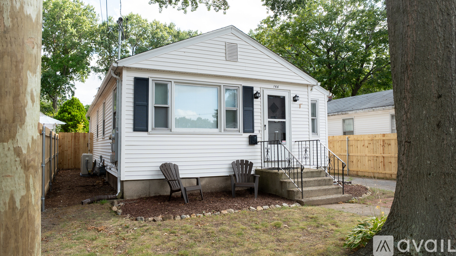 A small white house with a porch and a tree in front.