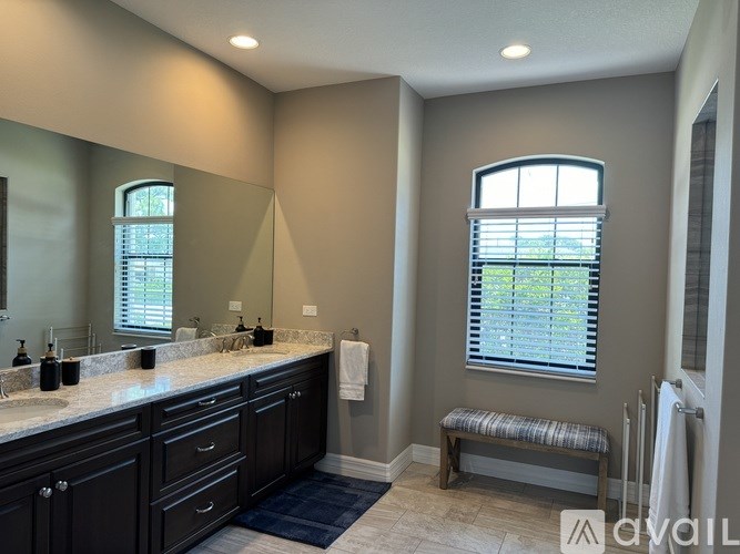 A bathroom with a large mirror, two sinks, and a window with blinds.