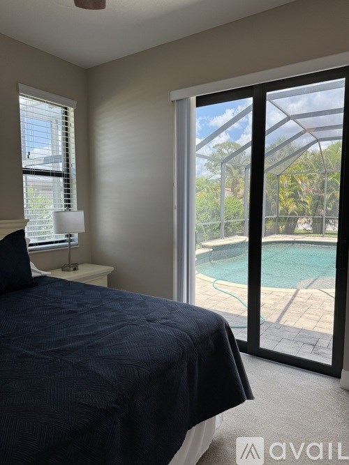 A bedroom with a large bed and a view of a pool through a sliding glass door.
