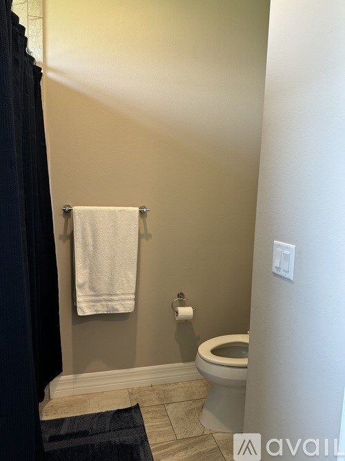 A bathroom with a toilet, a towel rack with a white towel, and a black shower curtain.