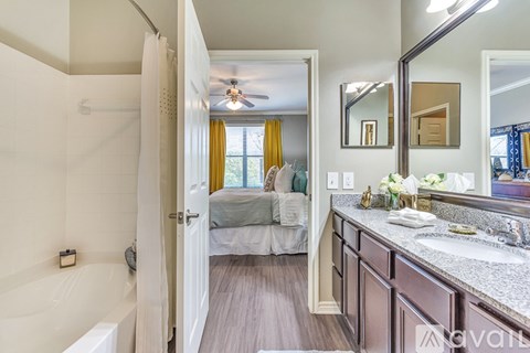 A bathroom with a white tub and a bedroom with a bed and a window.