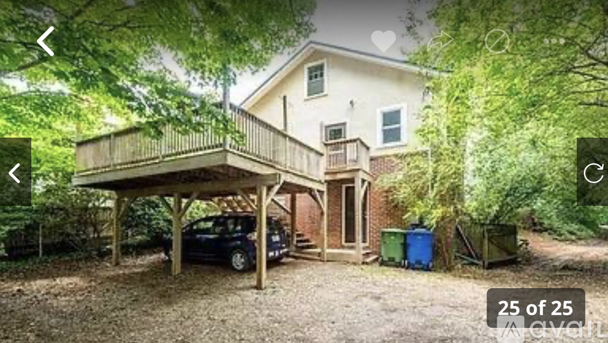 A car is parked under a wooden carport in a yard.