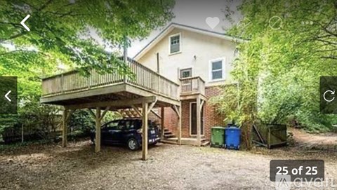 A car is parked under a wooden carport in a yard.