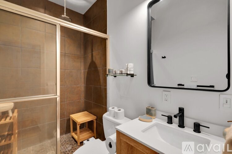 A bathroom with a brown tiled shower and white sink.
